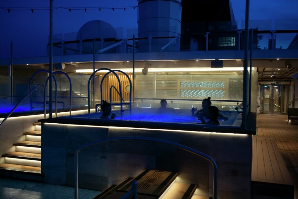 Schiffsdeck der MS Roald Amundsen bei Nacht mit einem Whirlpool im Vordergrund, stimmungsvolle blaue Beleuchtung.