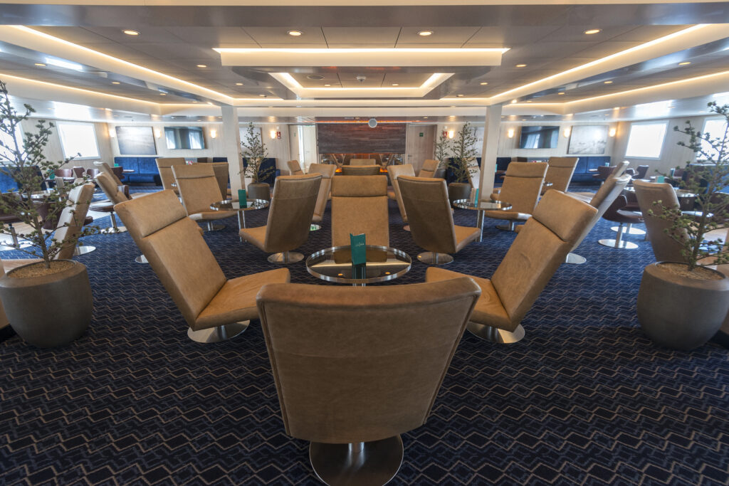 Explorer Bar MS Spitsbergen mit stilvollen braunen Loungesesseln um runde Glastische angeordnet, warmer einladender Raum
