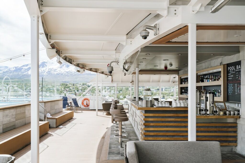 Pool Bar der MS Fridtjof Nansen. Rechts im Bild ist die überdeckte Bar mit hölzerner Theke zu sehen. Links sind Sitzgelegenheiten und im Hintergrund die schneebedeckten Berge zu sehen.