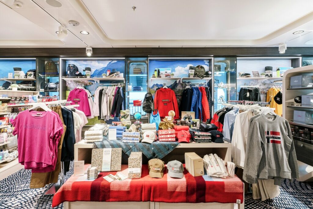 Im Vordergrund sind Regale, Tische und Kleiderständer zu sehen mit einer Vielzahl von Produkten wie Kleidung, Accessoires und Geschenken. 