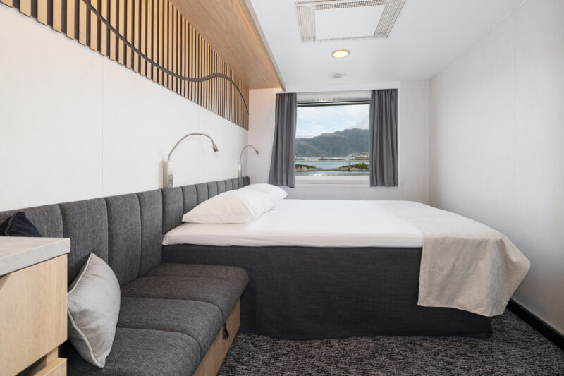 Helle Artic Außenkabine mit großem Fenster und Blick auf die Landschaft, ausgestattet mit einem Doppelbett, einer gepolsterten Sitzecke und moderner Einrichtung in warmen Holz- und Grautönen.