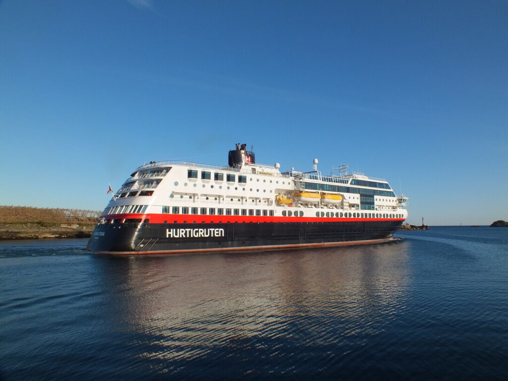 Das Schiff MS Midnatsol fährt bei strahlend blauem Himmel durch ruhiges Küstengewässer, klare Sicht auf Schiffsrumpf und Aufbau.