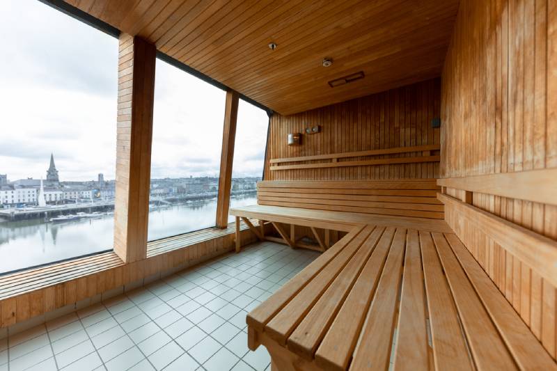 Sauna an Bord der MS Midnatsol mit großen Panoramafenstern und Blick auf das Meer, ausgestattet mit Holzbänken in mehreren Ebenen.