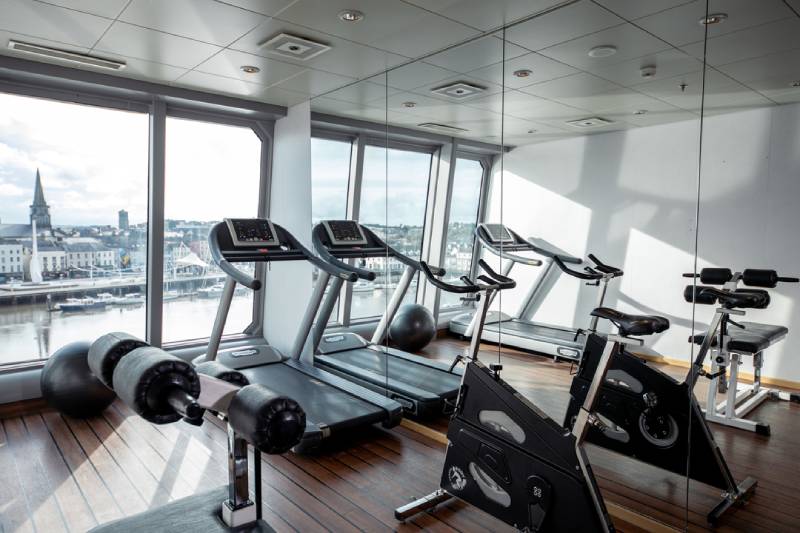 Fitnessraum mit Laufbändern, Ergometern und Panoramafenstern an Bord der MS Midnatsol.