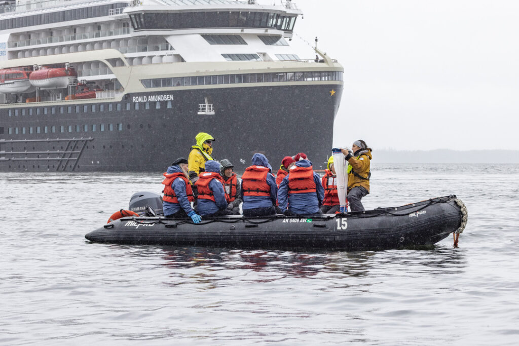 Ein Zodiac-Schlauchboot mit Passagieren in roten Schwimmwesten fährt nahe der MS Roald Amundsen durch die Gewässer der Kelp Bay in Alaska.