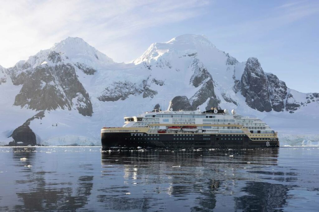 Das Expeditionsschiff MS Fridtjof Nansen fährt durch den Lemaire-Kanal in der Antarktis, umgeben von schneebedeckten Bergen und spiegelglattem Wasser.