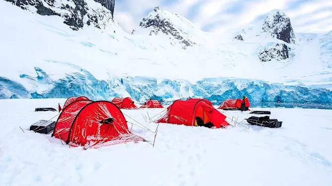 Rote HX-Expeditionszelte im Schnee vor einer eisblauen Gletscherkulisse in der Antarktis – Campingplatz unter extremen Bedingungen.