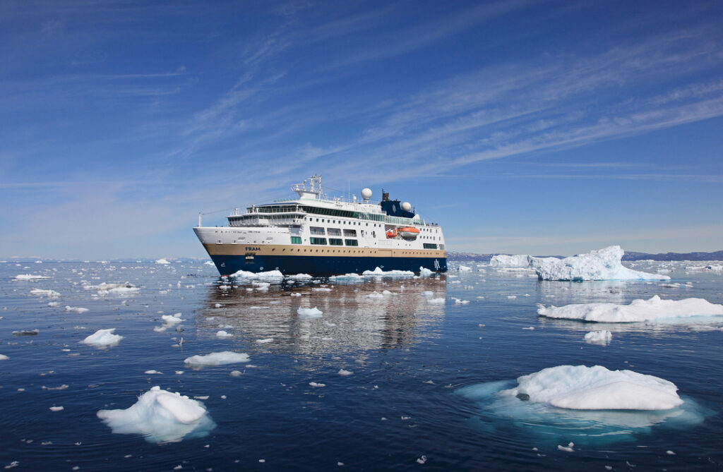 Das Expeditionsschiff MS Fram fährt durch die mit Eisschollen bedeckte Diskobucht in Grönland unter blauem Himmel mit leichten Wolken.