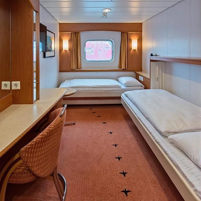 Polar Außenkabine (J2) mit Fenster an Bord der MS Midnatsol, zwei Einzelbetten entlang der Seitenwand, Schreibtisch mit Stuhl, Teppichboden und Holzverkleidung.