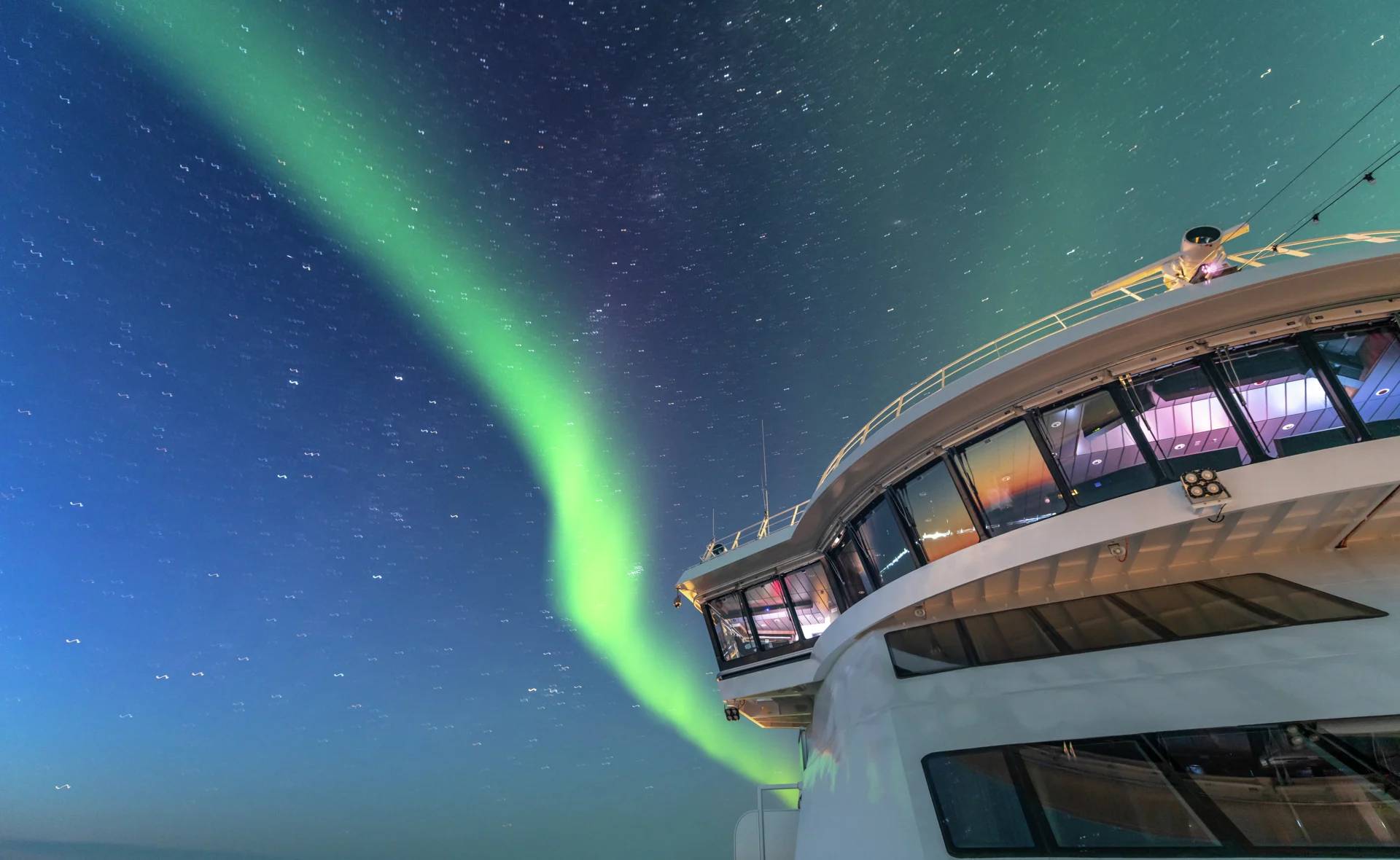 Das Oberdeck des Expeditionsschiffs MS Roald Amundsen unter dem Nachthimmel mit leuchtendem Polarlicht (Aurora Borealis) im Hintergrund.