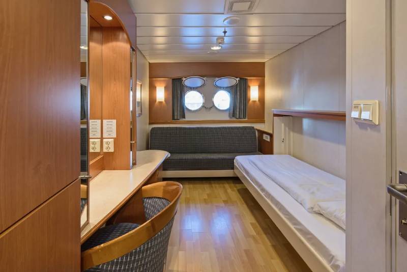 Helle Polar Außenkabine (L2) mit Bullaugen-Fenstern, seitlichem Einzelbett, Sofa, Schreibtisch und modernem Interieur in Holzoptik.