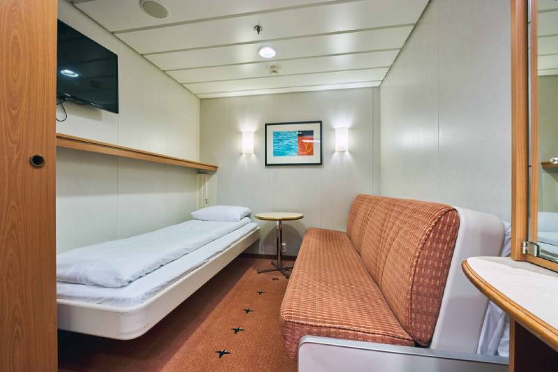 Komfortable Innenkabine an Bord der MS Midnatsol mit einem Einzelbett, einem Sofa, Wanddekor, Flachbildfernseher und kleinem Schreibtisch, modern und funktional eingerichtet.