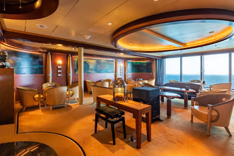 Panoramalounge an Bord der MS Midnatsol mit großen Fenstern, gemütlichen Sitzgruppen und stilvoller Beleuchtung.
