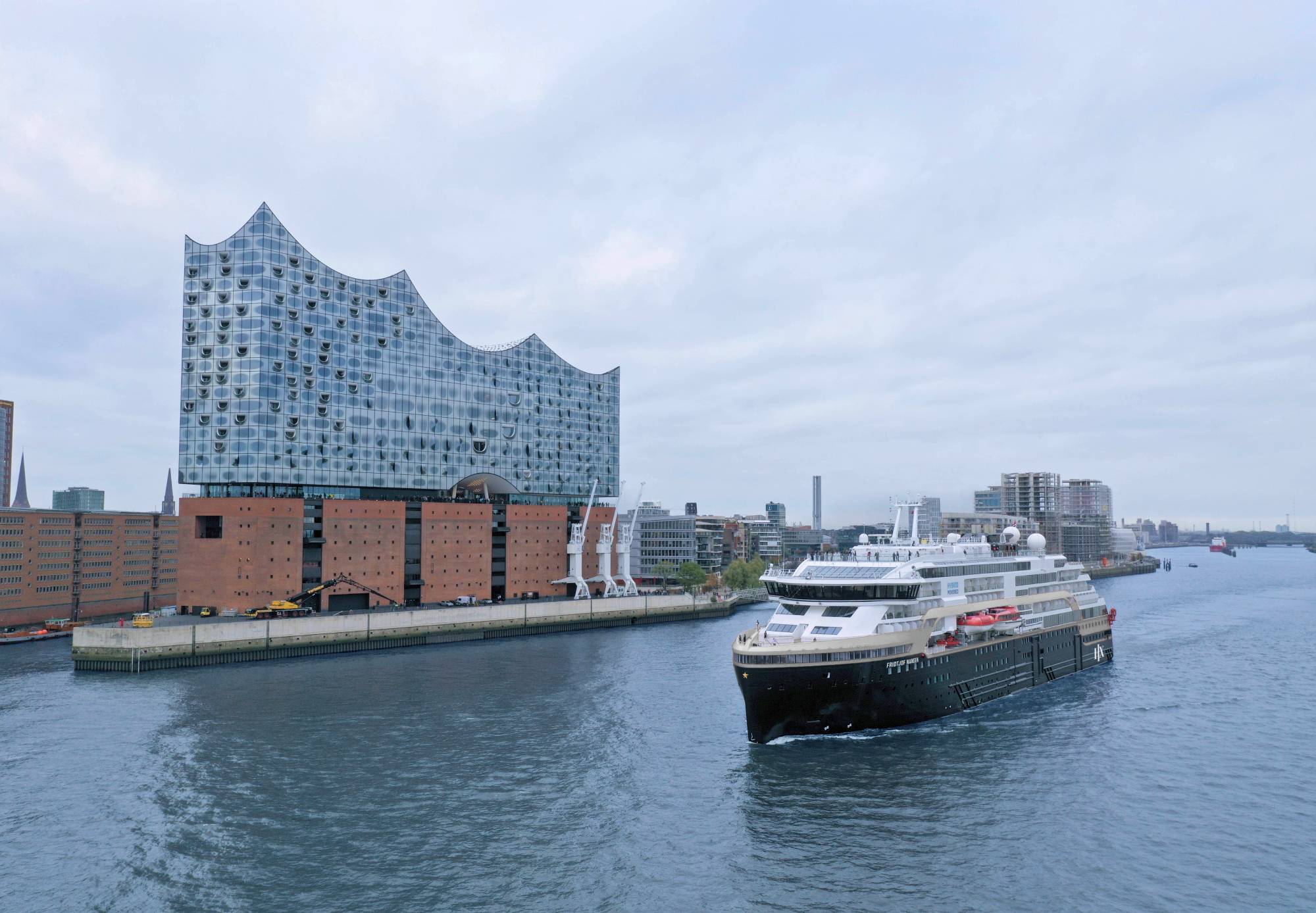 Die MS Fridtjof Nansen fährt an der Elbphilharmonie in Hamburg vorbei, bei bewölktem Himmel auf der Elbe.
