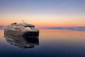 Das Expeditionsschiff MS Roald Amundsen fährt bei Sonnenuntergang durch spiegelglattes Wasser in polarer Umgebung.