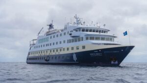 Das Expeditionsschiff MS Santa Cruz II fährt bei bewölktem Himmel durch ruhige Gewässer, frontal von der Steuerbordseite aufgenommen.