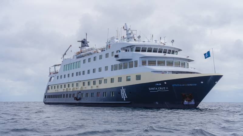 Das Expeditionsschiff MS Santa Cruz II fährt bei bewölktem Himmel durch ruhige Gewässer, frontal von der Steuerbordseite aufgenommen.