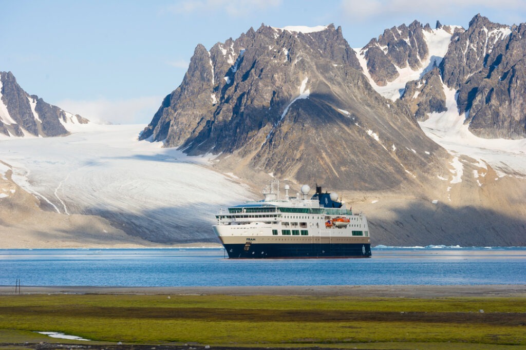 Das Expeditionsschiff MS Santa Cruz II liegt vor einer dramatischen arktischen Bergkulisse mit Gletschern und grünem Küstenvorland.