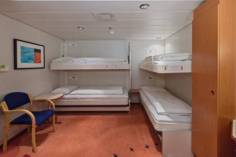 Vierbett-Innenkabine an Bord der MS Midnatsol mit Etagenbetten, Sitzgelegenheit, Wanddekor und einfachem Stauraum in funktionalem Design.