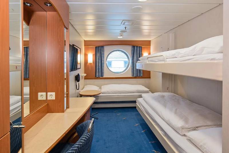 Polar Außenkabine (J3) mit Bullaugen-Fenster, zwei unteren Einzelbetten und einem oberen Klappbett, Schreibtisch und blauem Teppichboden.