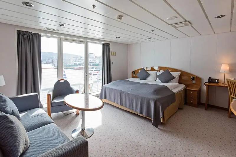 Komfortable Suite (M2) mit Doppelbett, Sitzecke, bodentiefen Fenstern und privatem Balkon an Bord der MS Midnatsol.